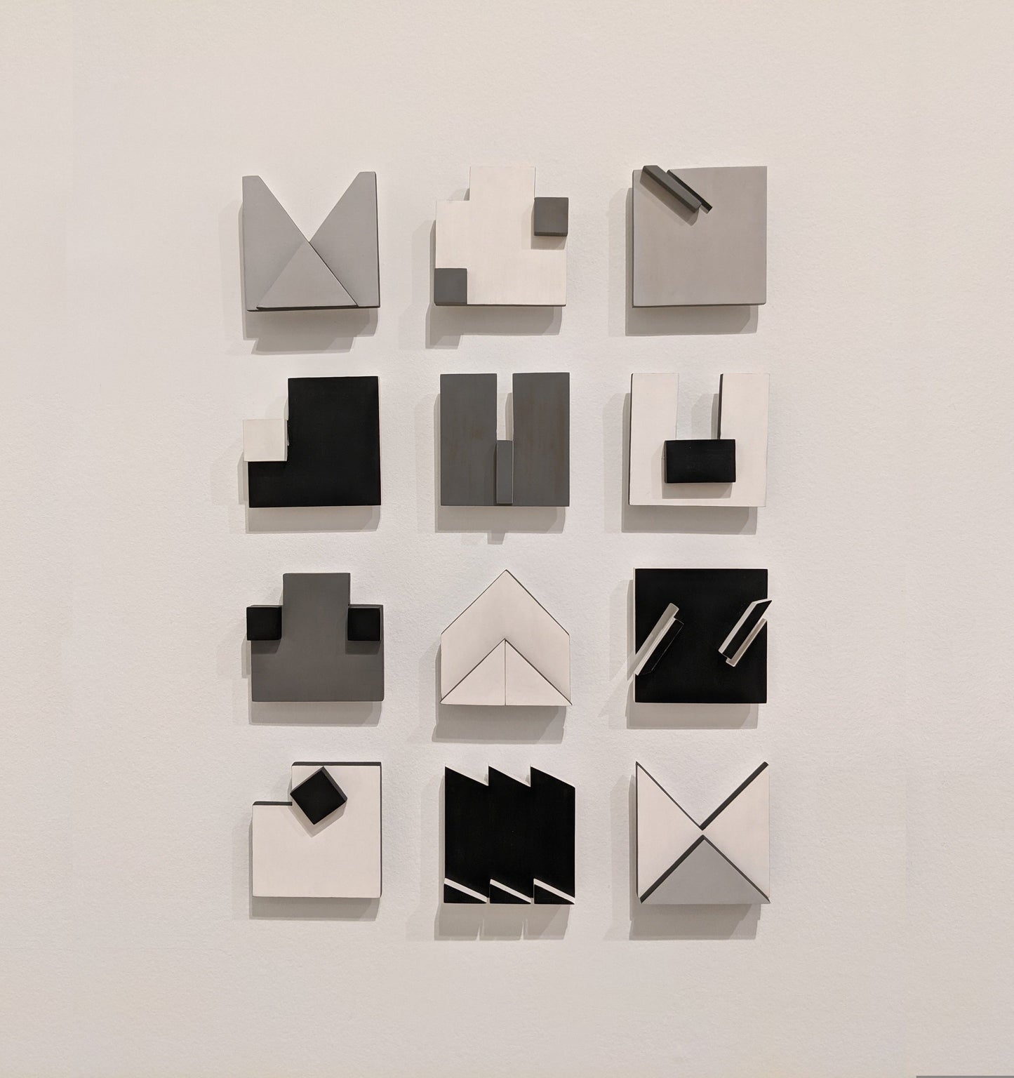 A grid of abstract geometric wall art in shades of black, white, and gray, featuring various shapes and arrangements.