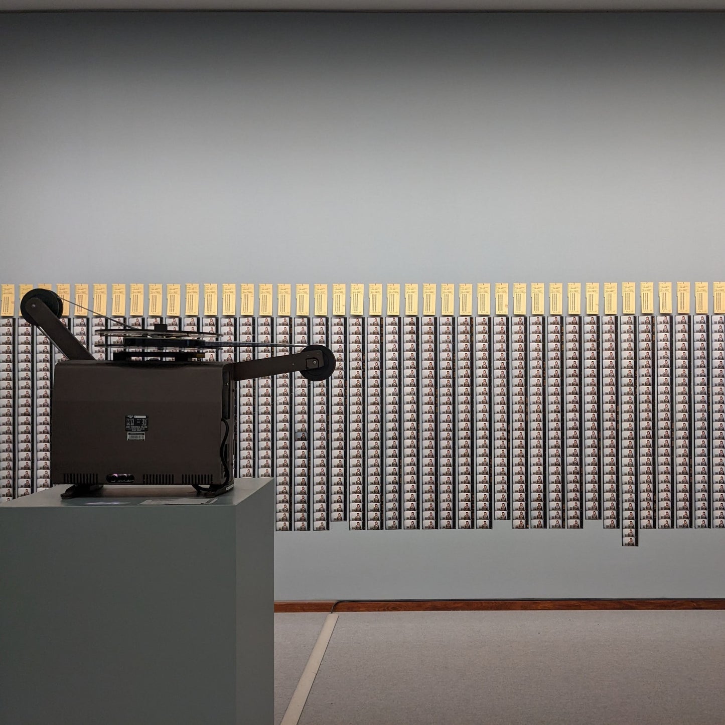 A vintage film projector displays iconic black and white film strips lined with yellow tags on the wall.
