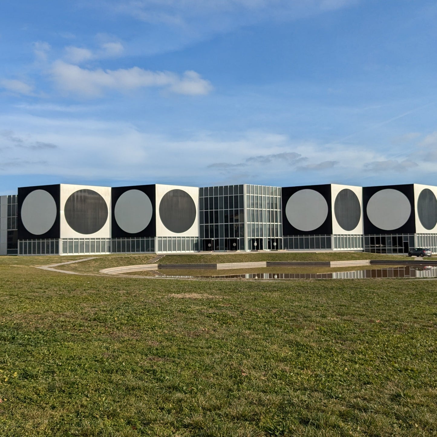 Modern building with large white circles on a black facade, surrounded by green grass and a clear blue sky.