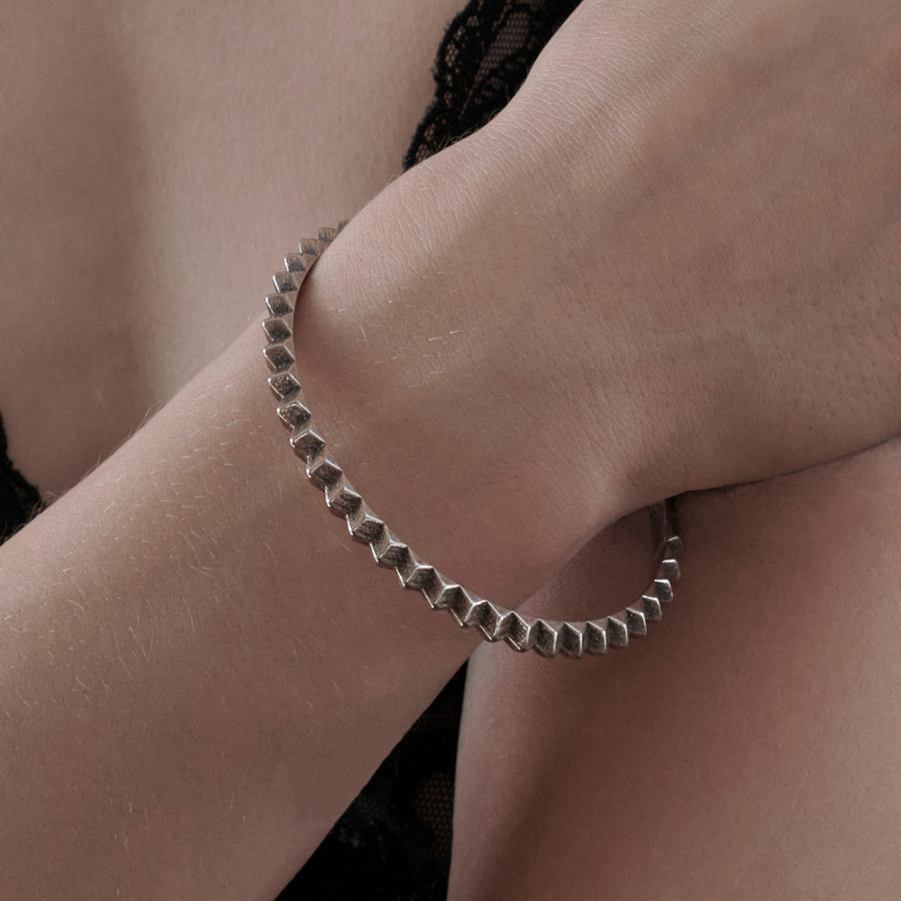 A close-up of a wrist adorned with a geometric silver bracelet, set against a backdrop of delicate black lace.