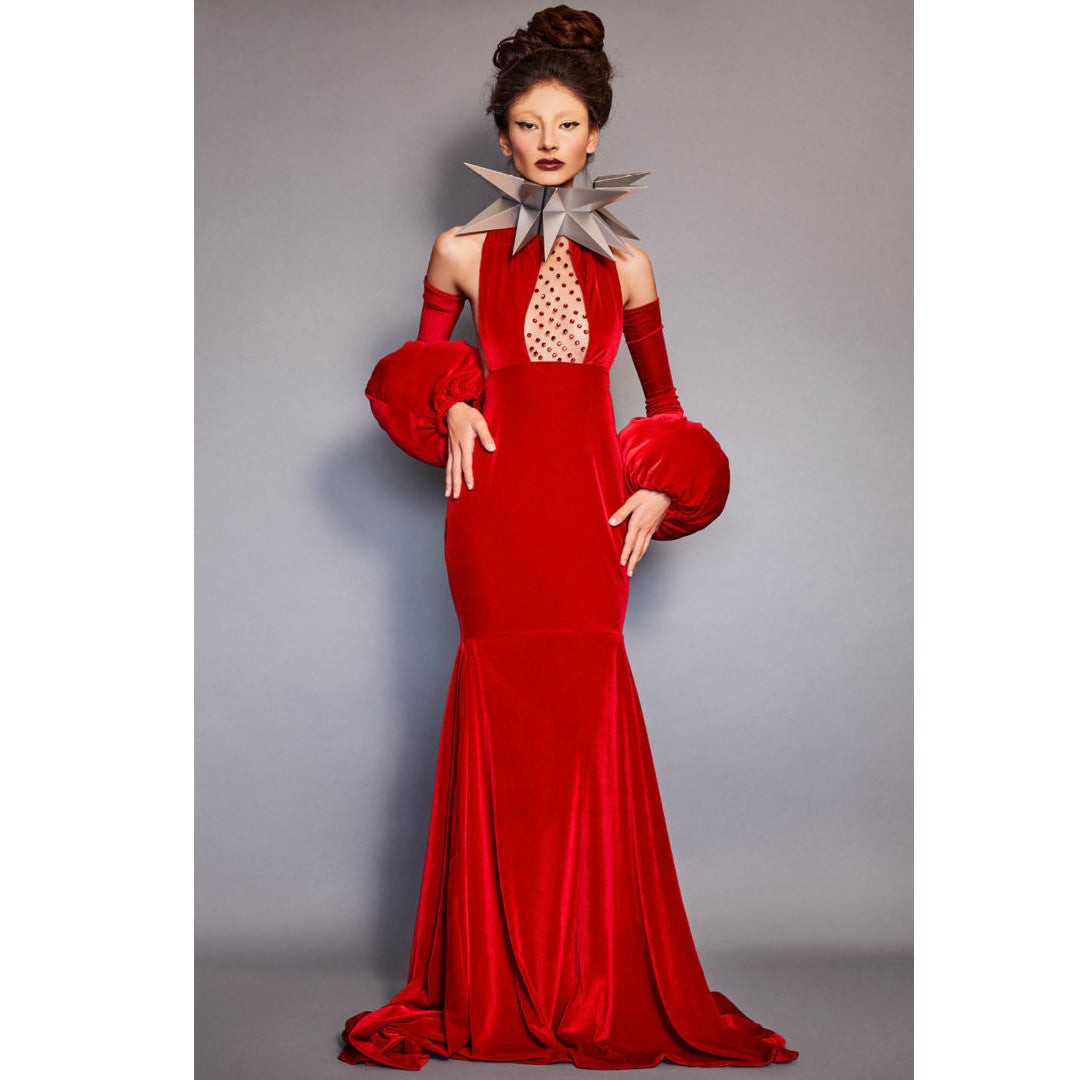A model wears a striking red velvet gown with dramatic puffed sleeves and a star-shaped neckline, featuring a polka dot cutout and silver geometric oversized necklace.