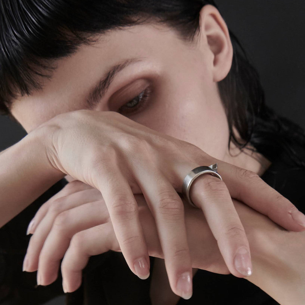A close-up of two hands resting on a dark surface with glossy nails and a stylish ring.