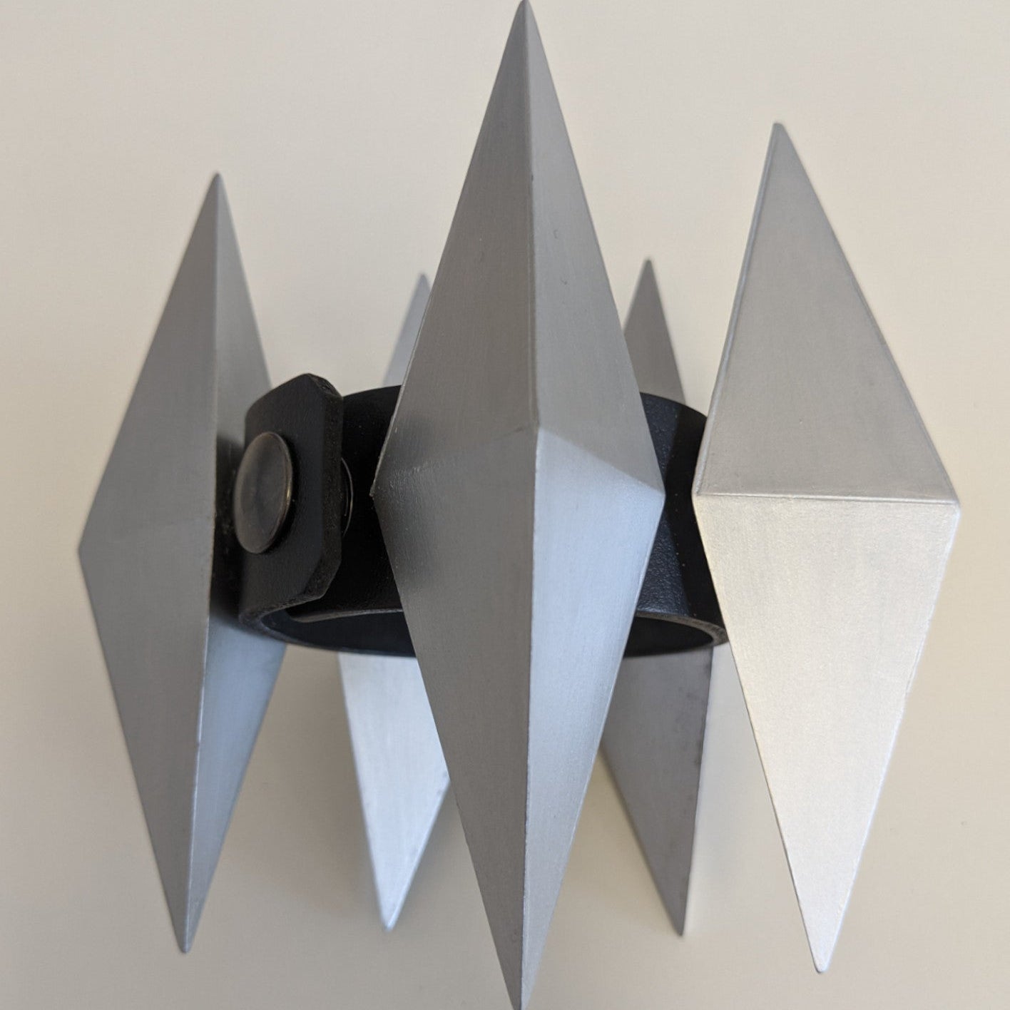 A silver spike bracelet featuring four triangular spikes, attached to a black leather band with a metal snap closure.