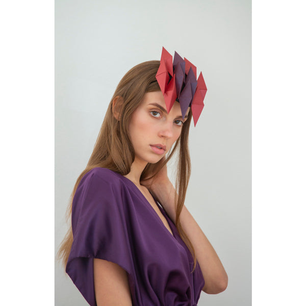 A woman with long brown hair wearing a purple dress and headpiece with ten red and purple pyramids. 