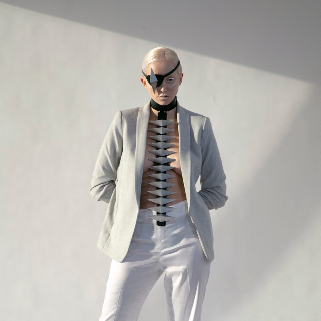 A model stands confidently in a stylish light gray blazer and white trousers, showcasing a striking design element through the open blazer.