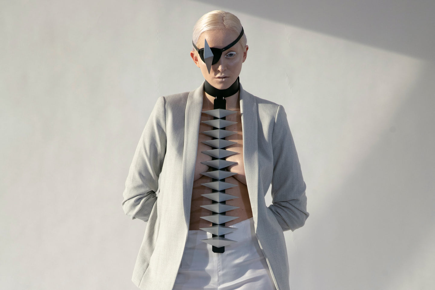 A model stands confidently in a stylish light gray blazer and white trousers, showcasing a striking design element through the open blazer.