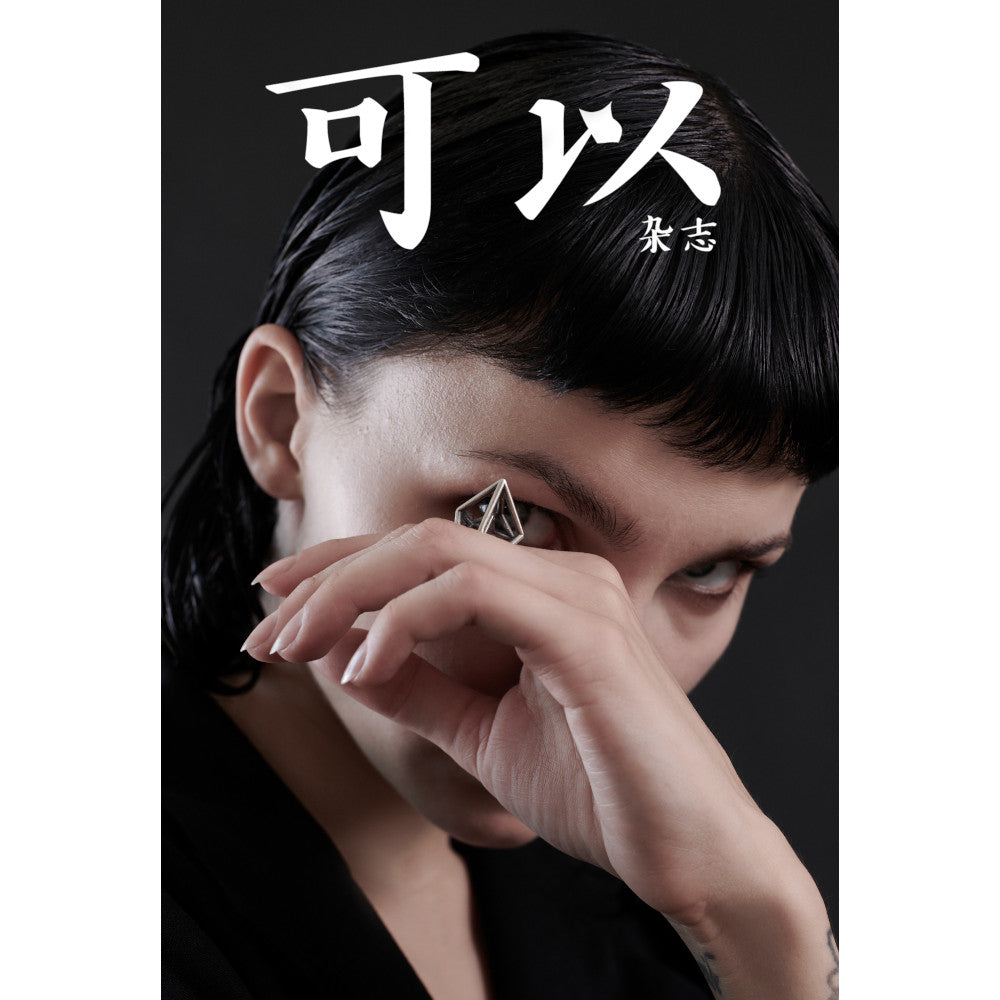Close-up of a woman's hand in front of her face, wearing a large, geometric ring, with a blurred black jacket background and white Chinese letters.