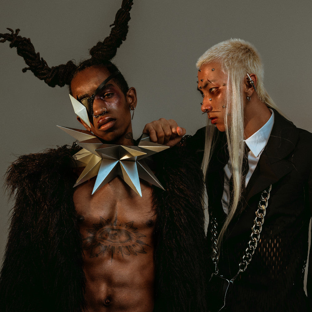 Two stylized individuals wear striking fashion pieces, featuring a dramatic star-shaped collar and a textured black fur garment.