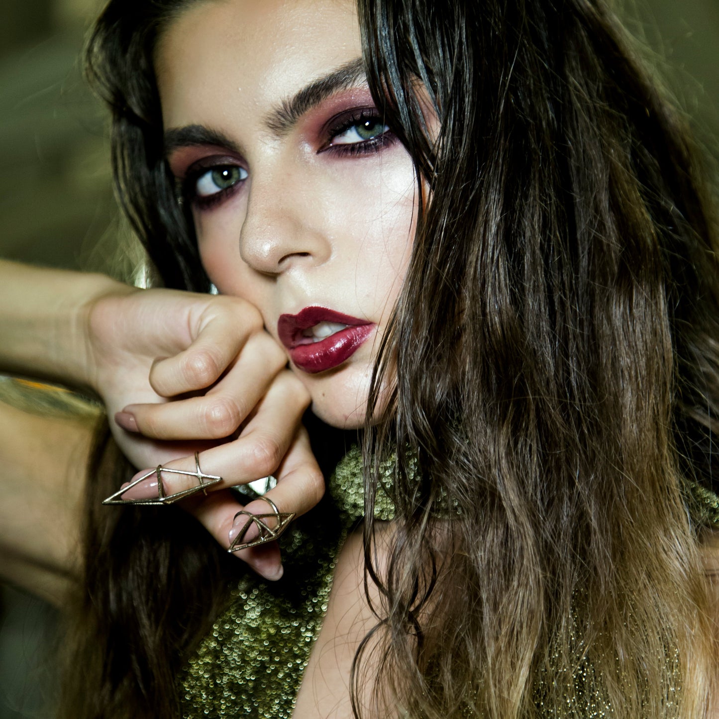 A close-up of a woman with her hand resting against her face, wearing two geometric rings.
