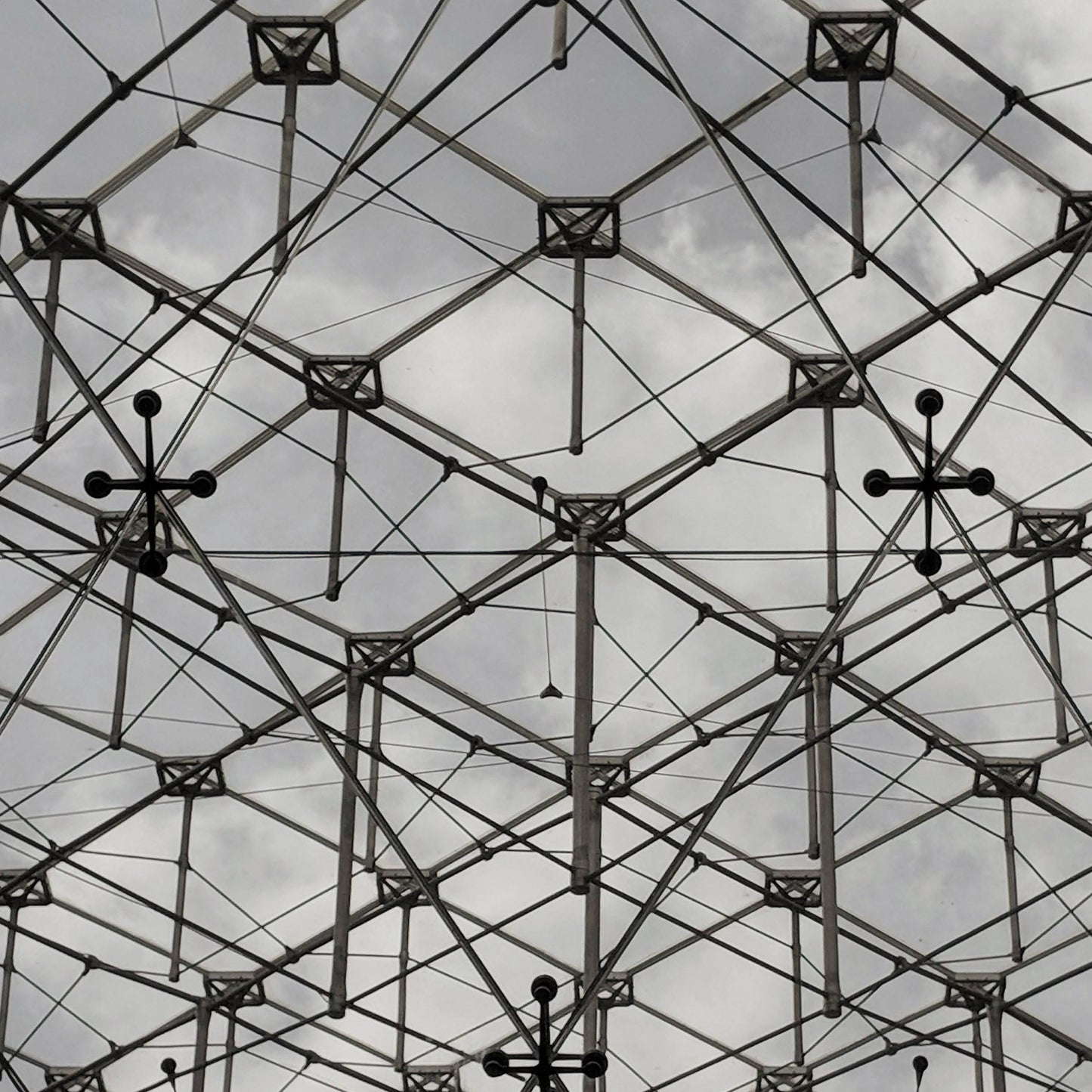 Abstract view of a geometric lattice structure against a cloudy sky, highlighting its interconnected framework and industrial design.