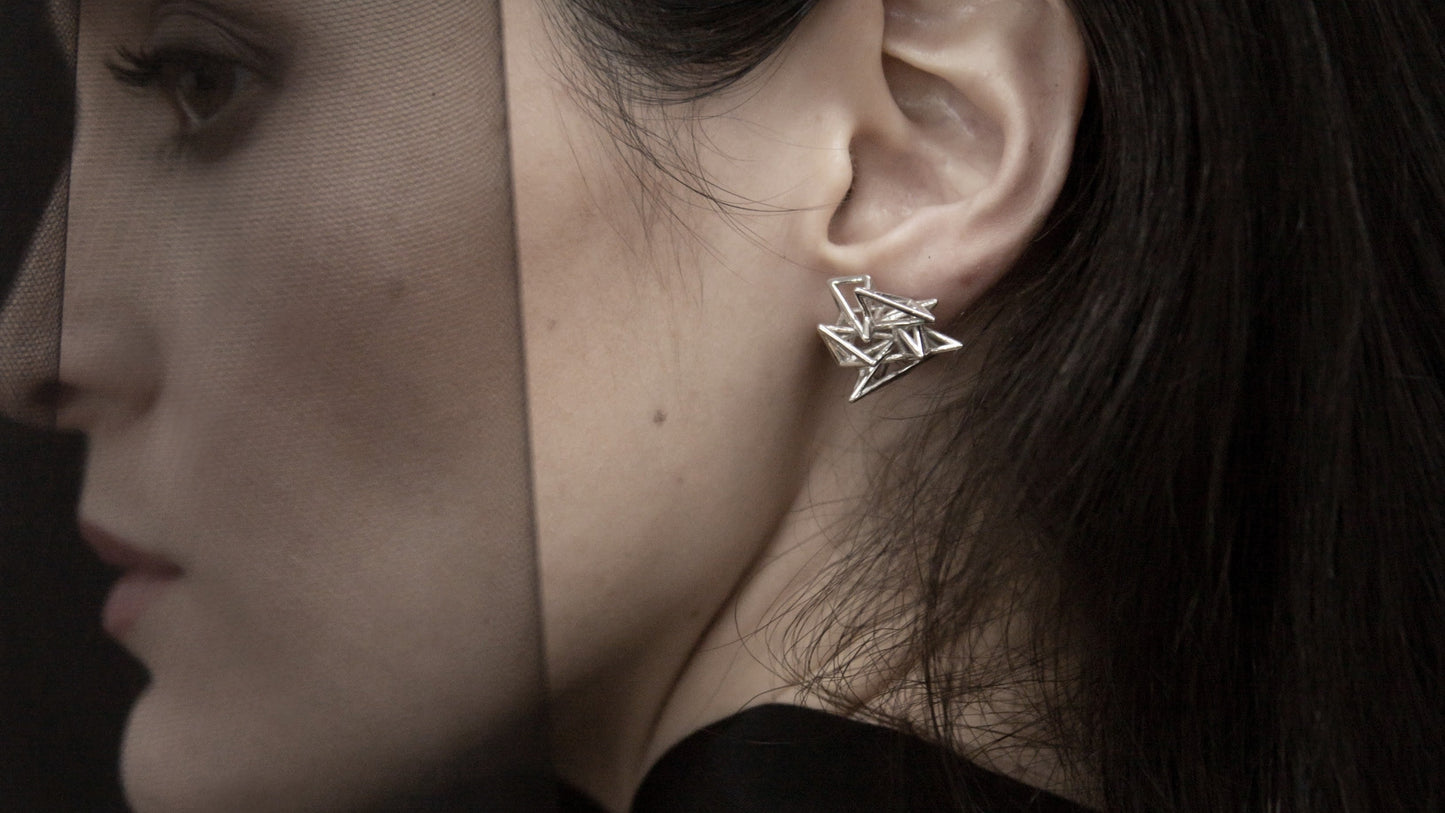 Close-up of a silver geometric star earring worn on the left ear, contrasting against dark hair and clothing.