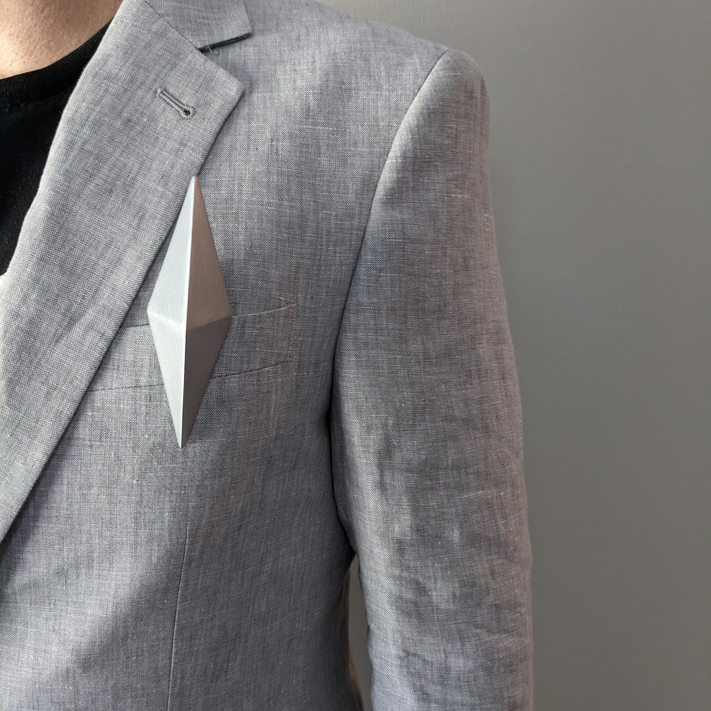 A man's torso wearing a grey blazer with a silver geometric pin on the front.