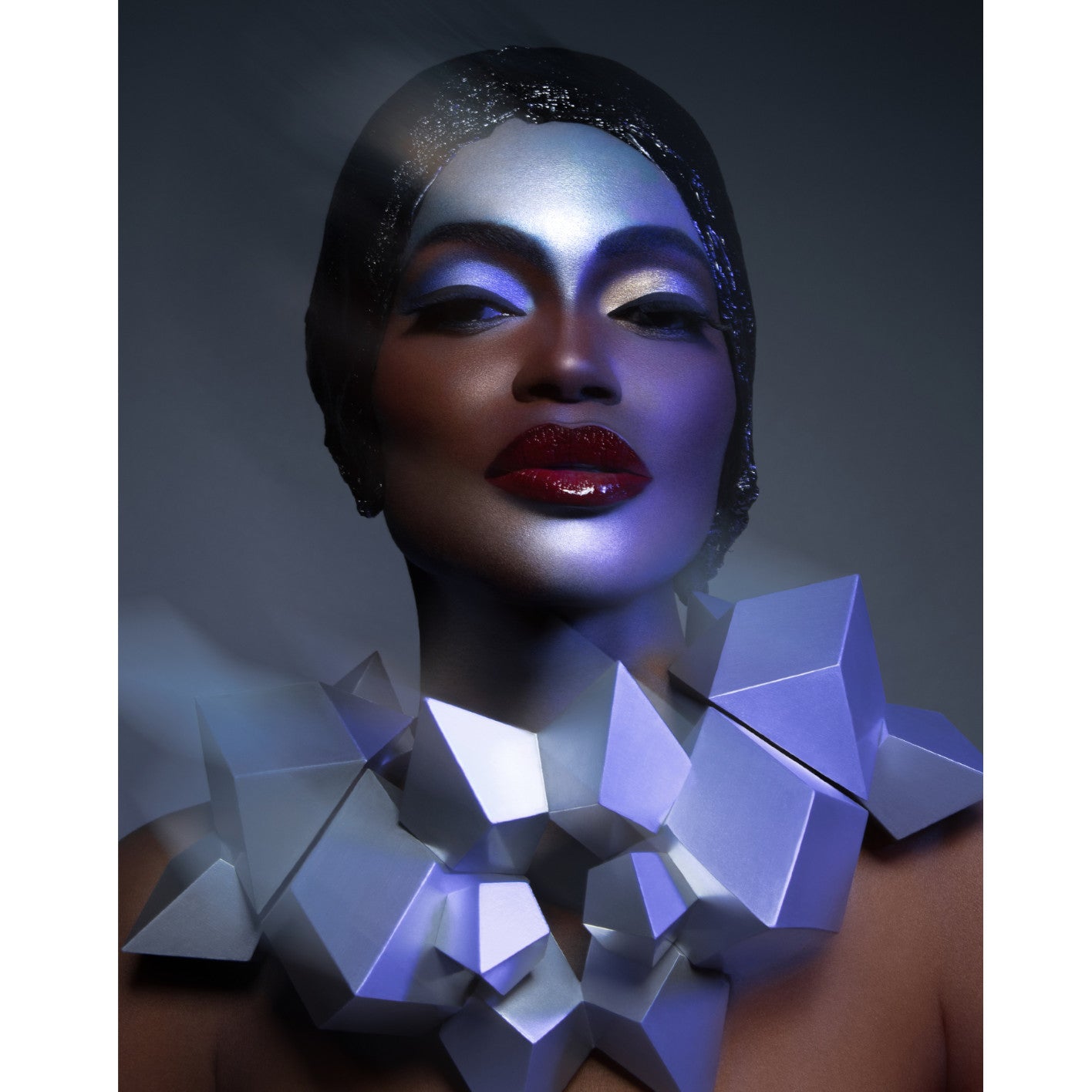 An abstract necklace made of geometric shapes in shades of white and purple is worn, set against a dark, muted background.