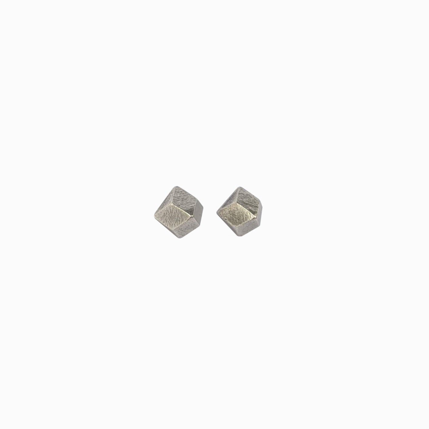 Two geometric silver studs with a textured surface, reflecting light, set against a white background.