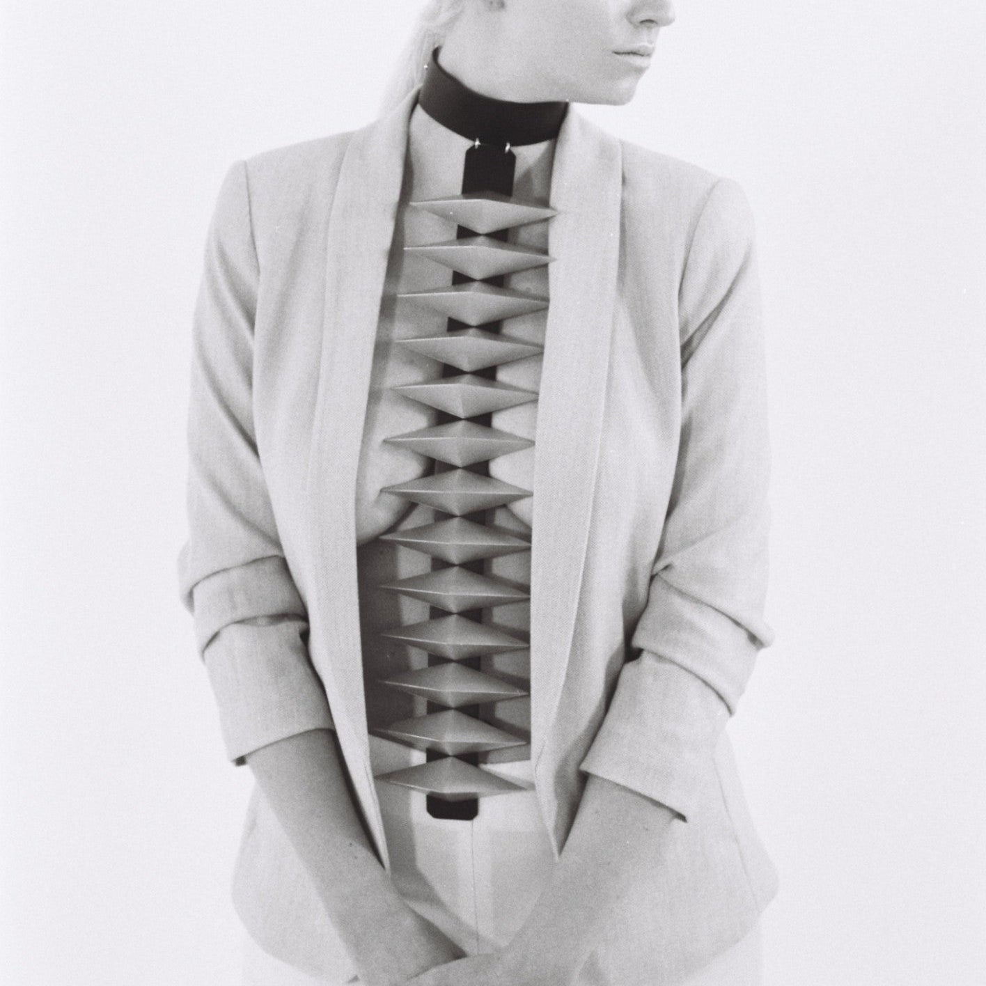 A person in a tailored light-colored blazer with a unique, structured cutout design on the torso area, styled against a minimalist background.