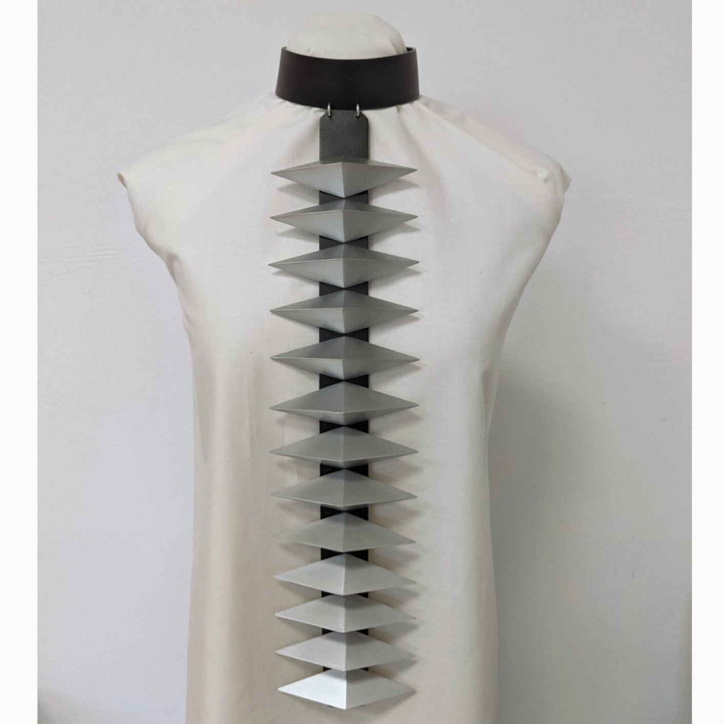 A fashion design on a mannequin features a unique gray and black statement necklace with layered, triangular elements.