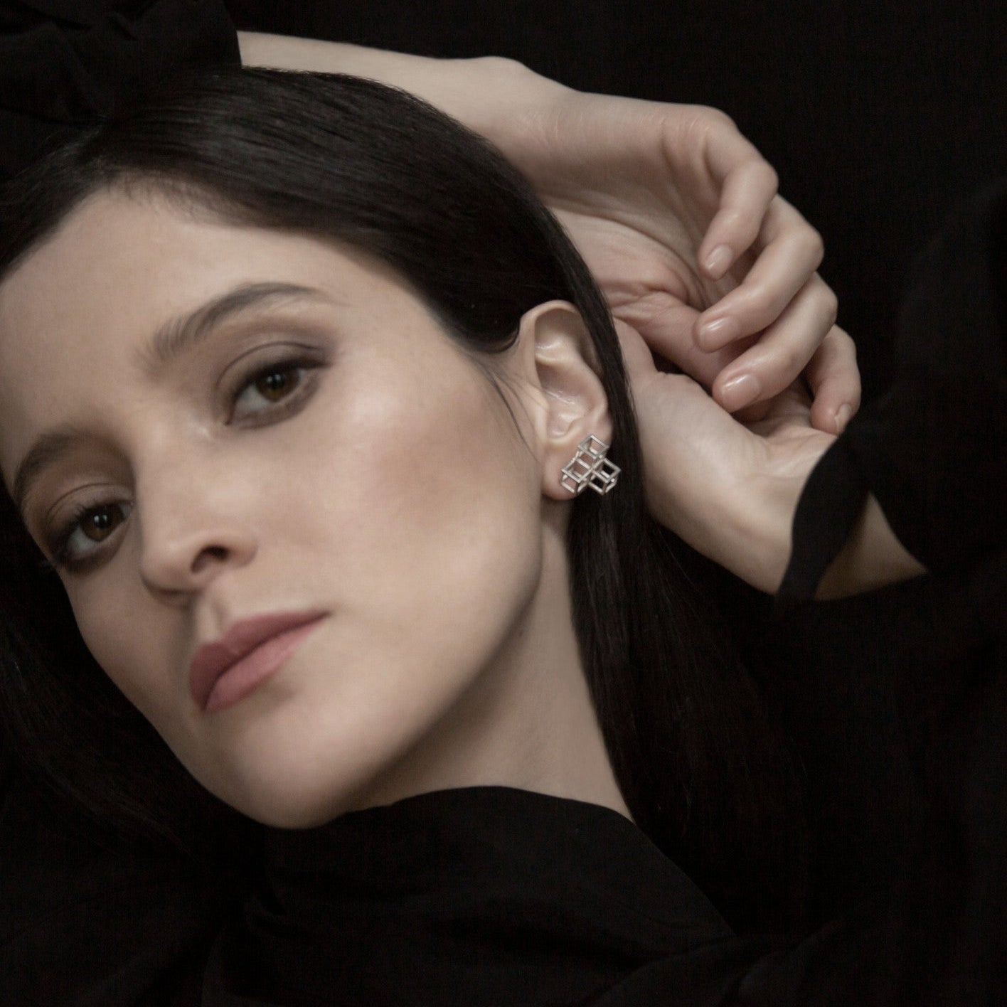 A close-up of a hand delicately holding a long, straight black hair, showcasing a stylish silver earring against a dark background.