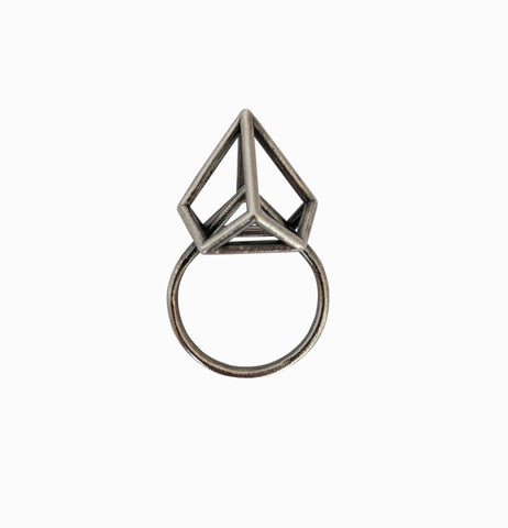 A silver ring with a geometric, triangular prism design set atop the band, isolated on a white background.