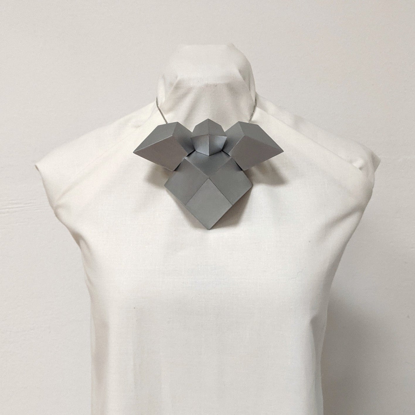A sculptural, geometric silver necklace displayed on a dress form, featuring angular shapes and a modern design.