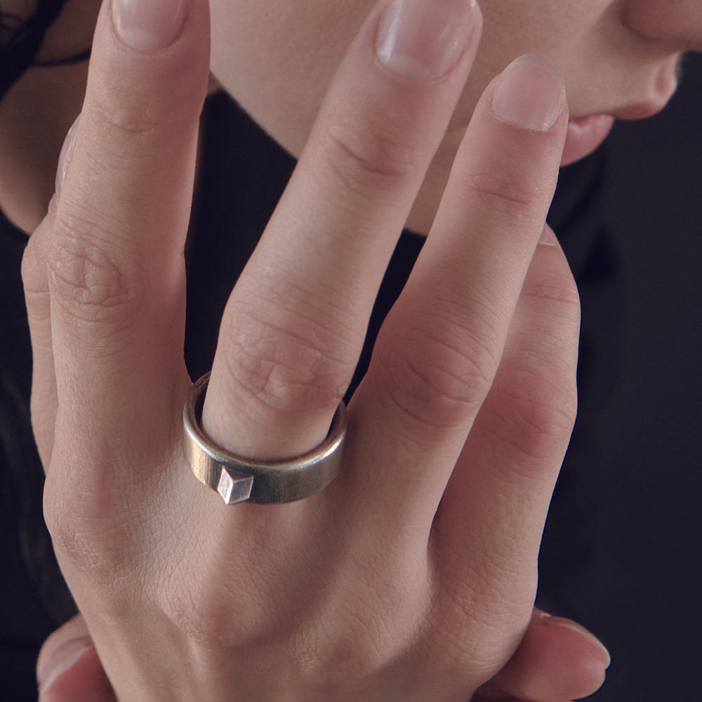 A close-up of a person's hand showcasing a unique metallic ring with a geometric shape, against a dark background.