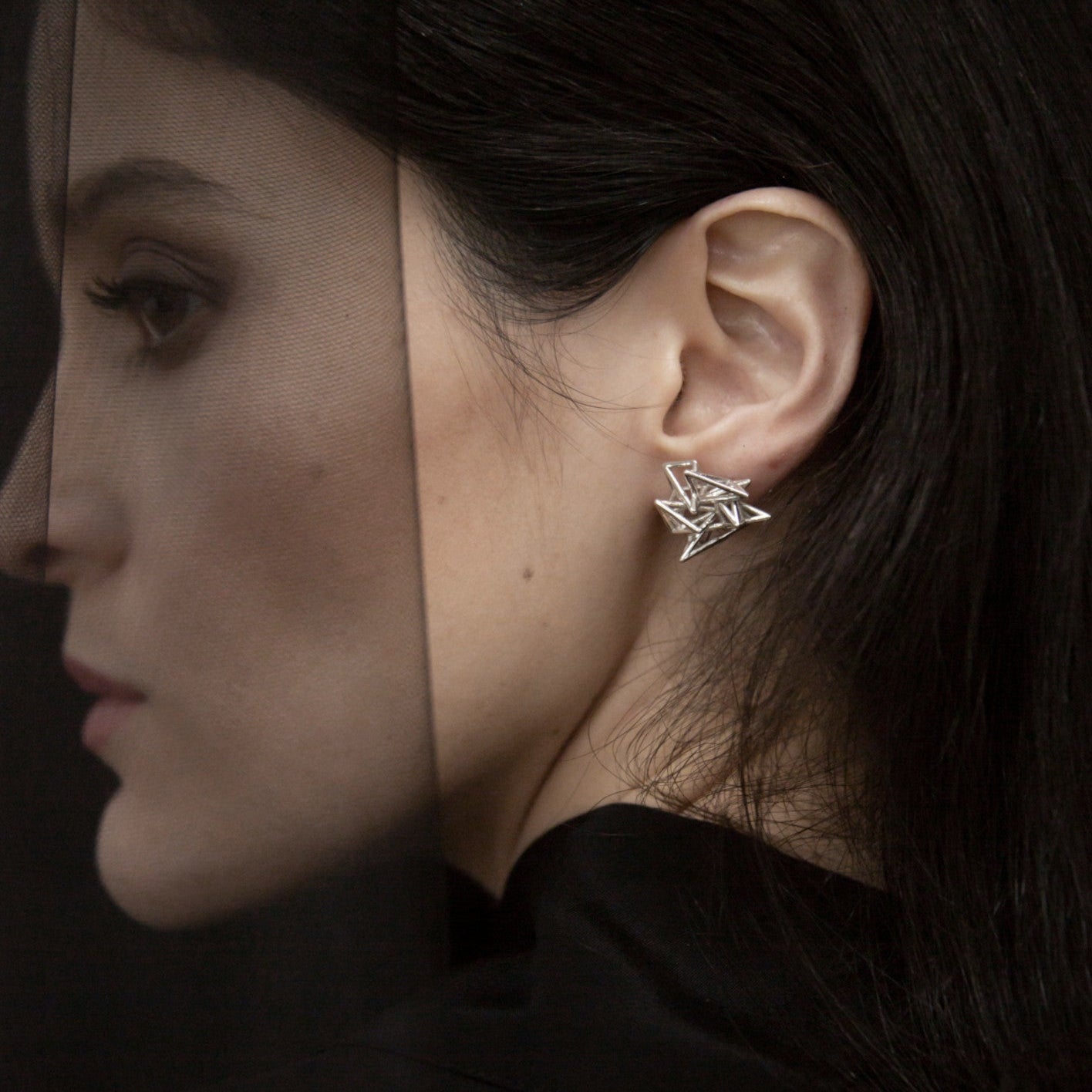 Close-up of a silver geometric star earring worn on the left ear, contrasting against dark hair and clothing.