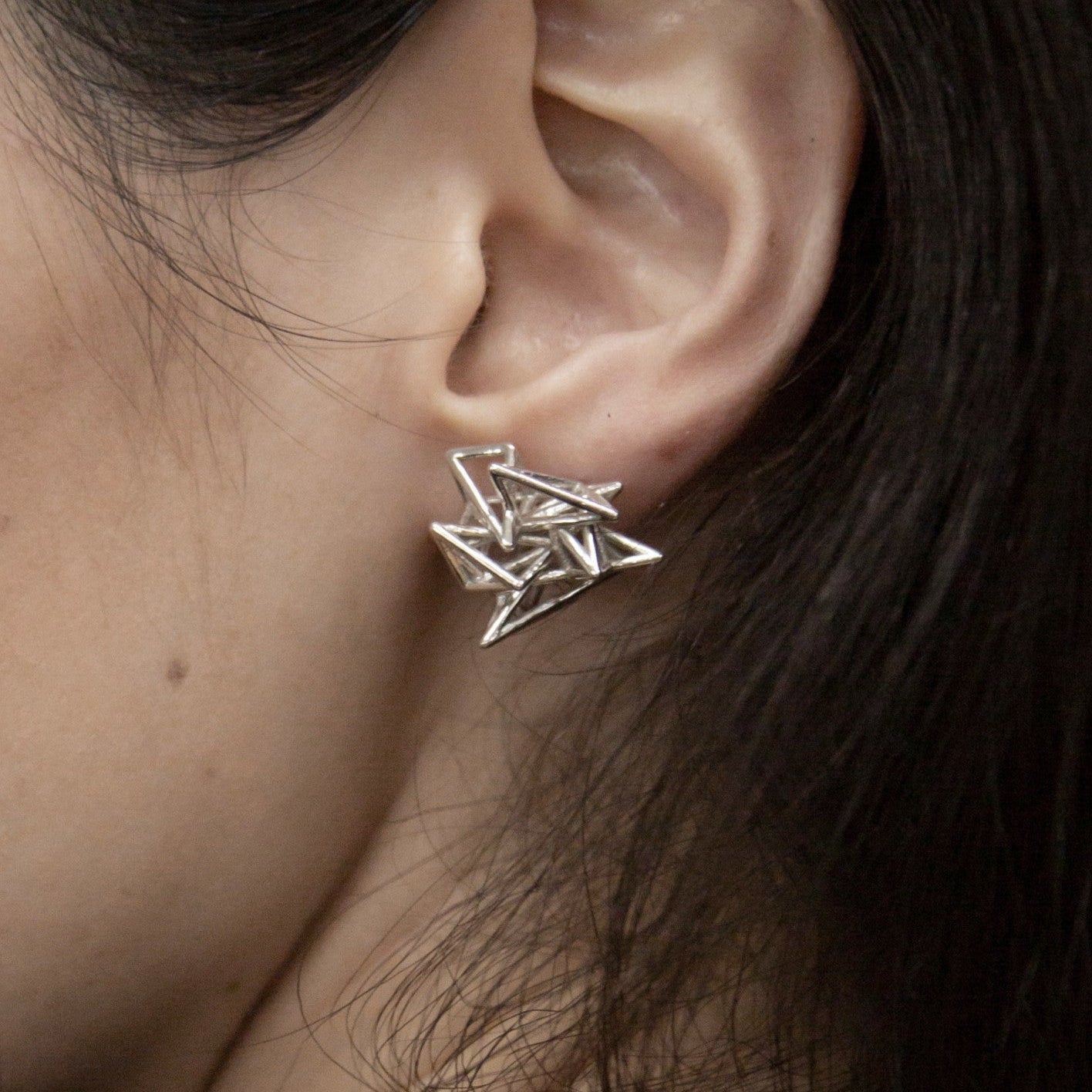 Close-up of a woman's ear showcasing a geometric silver earring with sharp, angular designs.