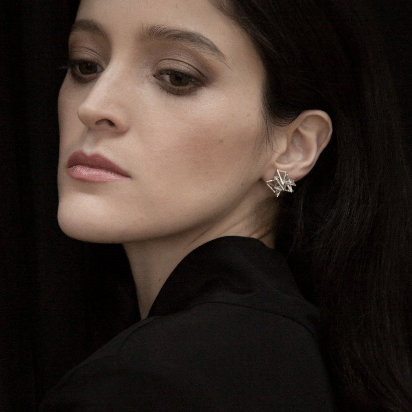 A close-up of a person wearing a stylish silver star-shaped earring, set against a dark background.