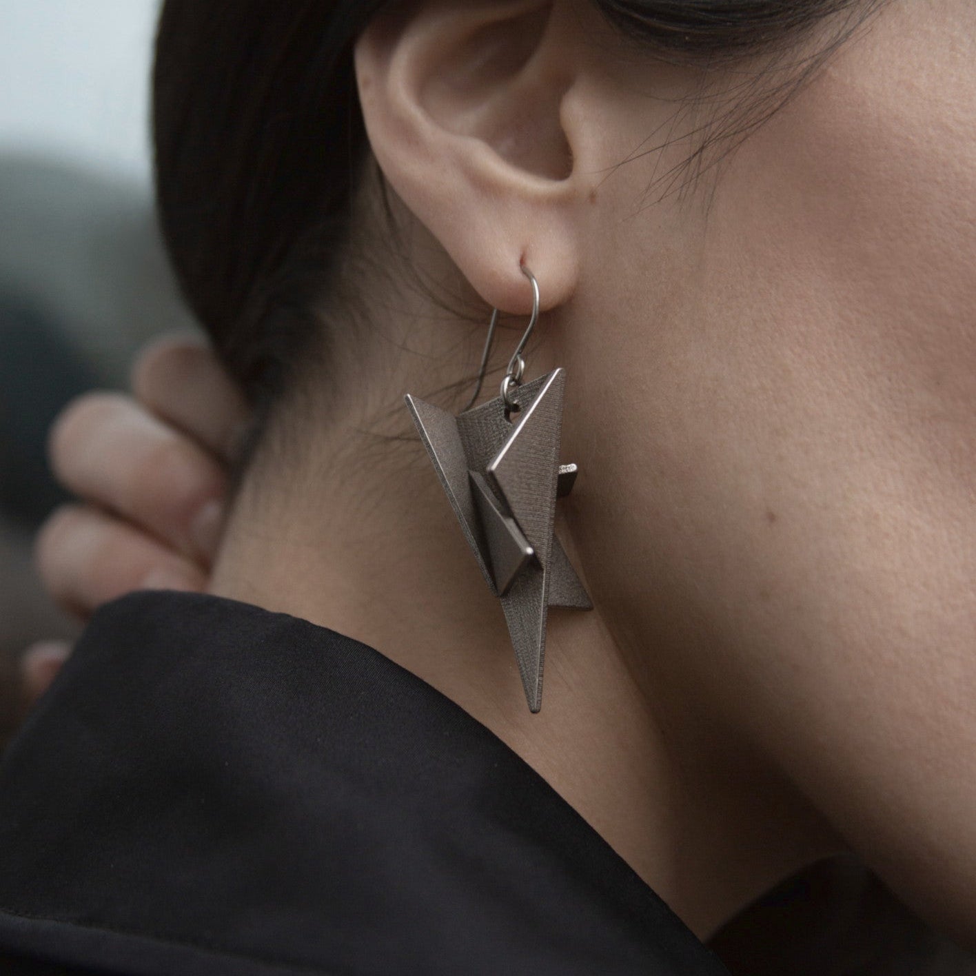 Close-up of a woman's ear adorned with a striking geometric silver earring, showcasing intricate, modern design elements.