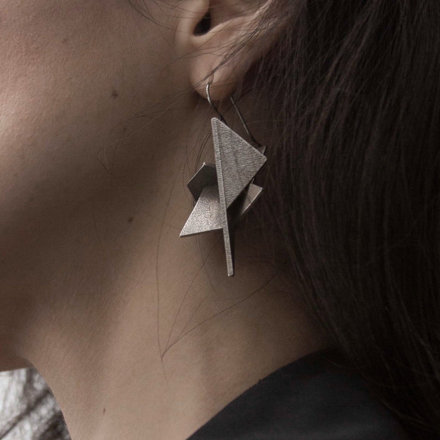 Close-up of a woman's ear adorned with a striking geometric silver earring, showcasing intricate, modern design elements.