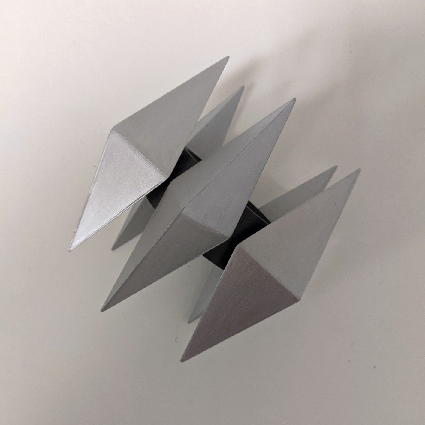 A geometric sculpture featuring four metallic pyramids arranged symmetrically around a central axis.