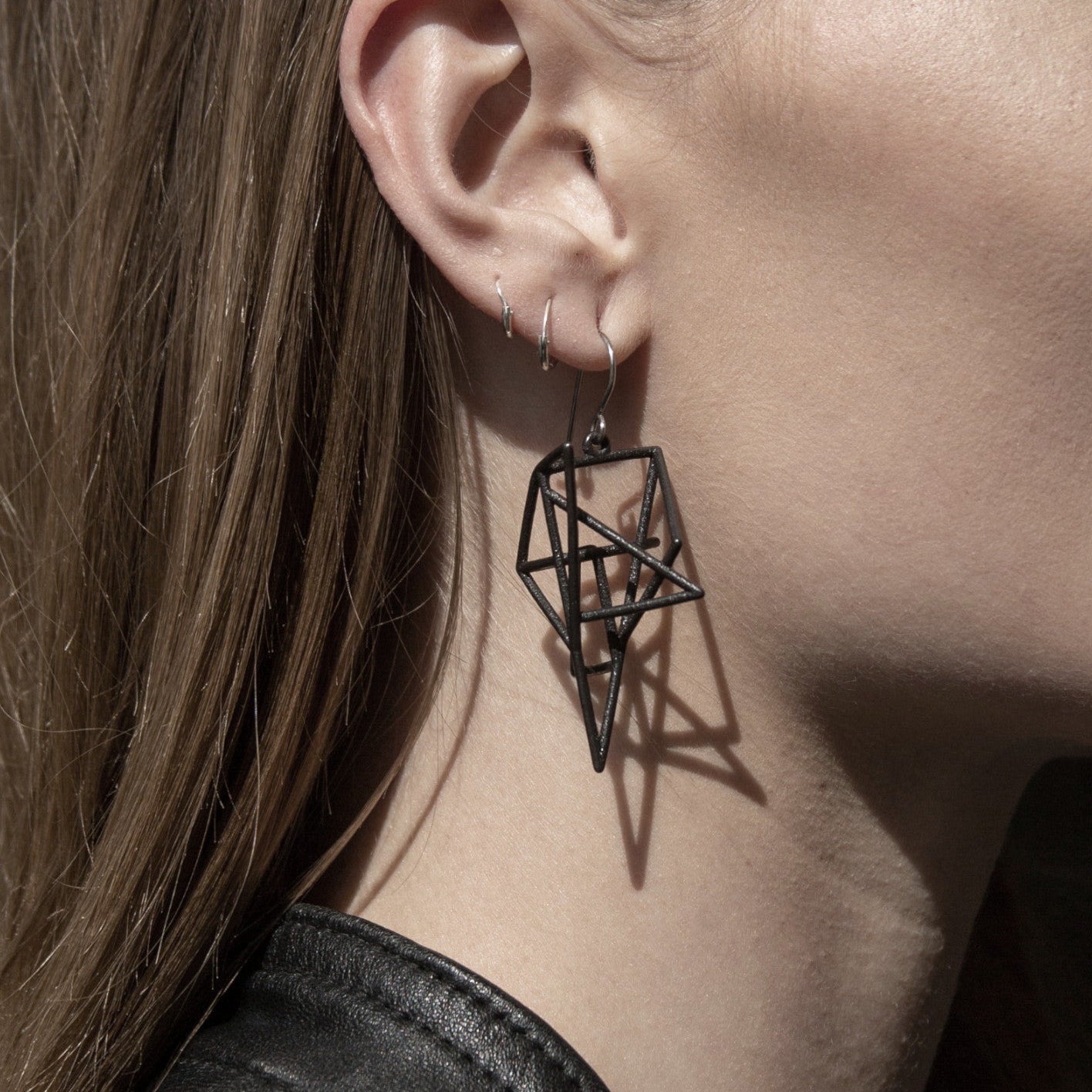 A close-up of a woman’s ear showcasing a striking black geometric earring, casting intricate shadows on her skin.