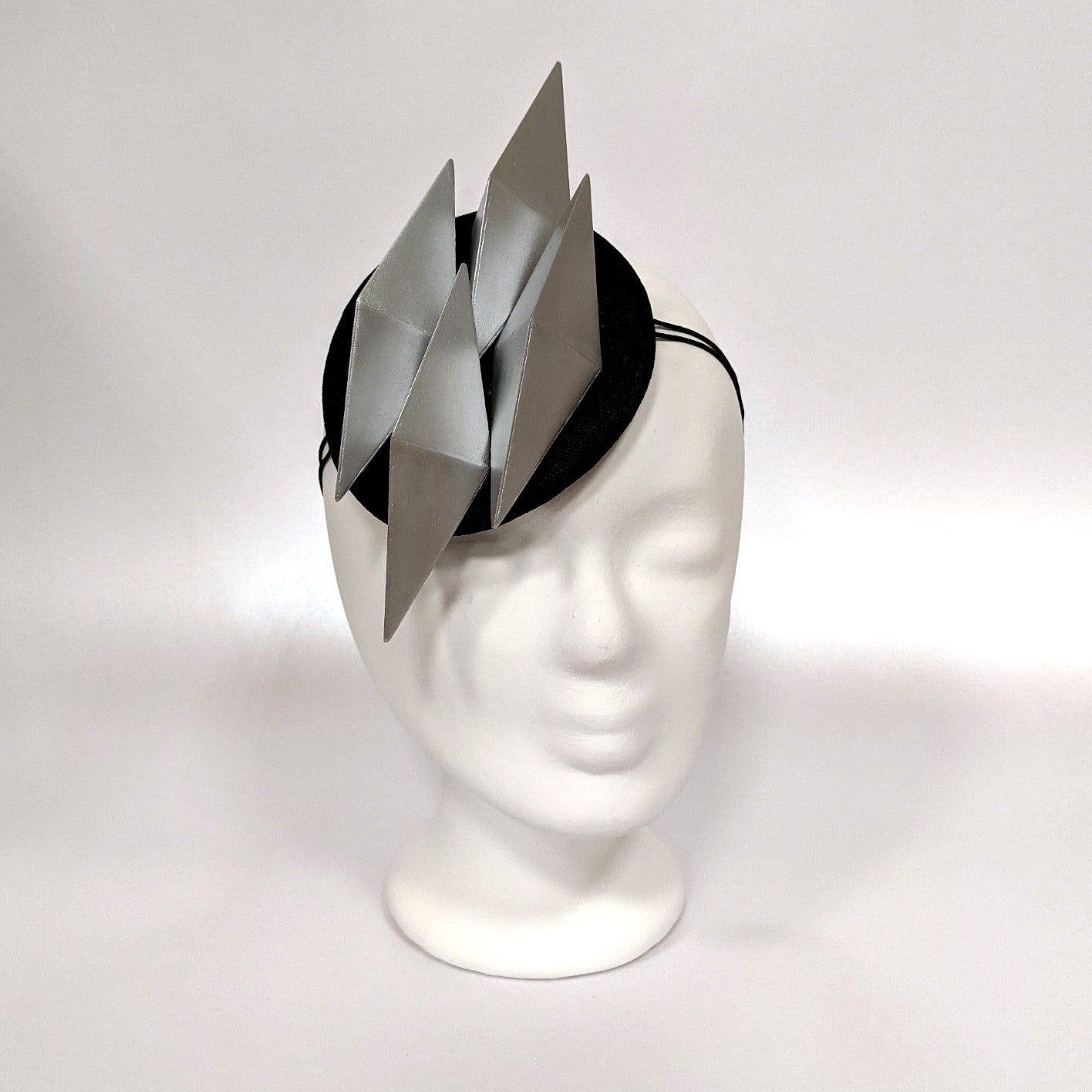 A black headband features three metallic silver triangular spikes, presented on a white mannequin head against a light background.