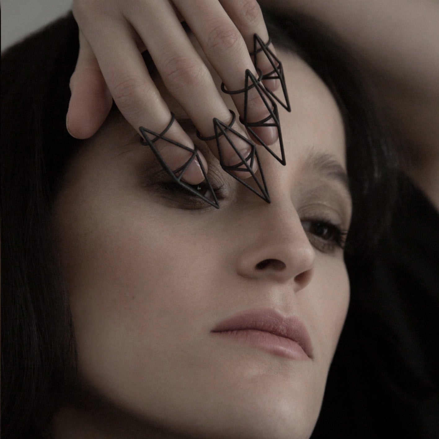 A close-up of a person with hints of dark hair and a hand positioned above wearing geometric rings, suggesting a casual, intimate moment.