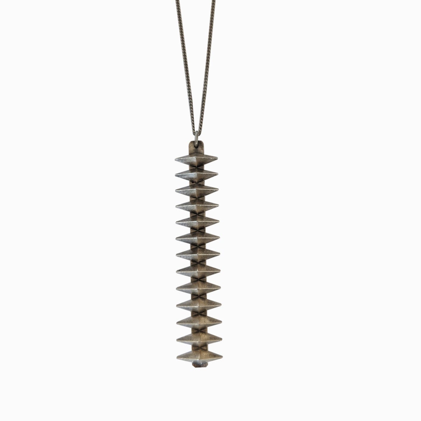 A vertical, textured silver pendant with a tiered design, suspended from a delicate chain against a white background.