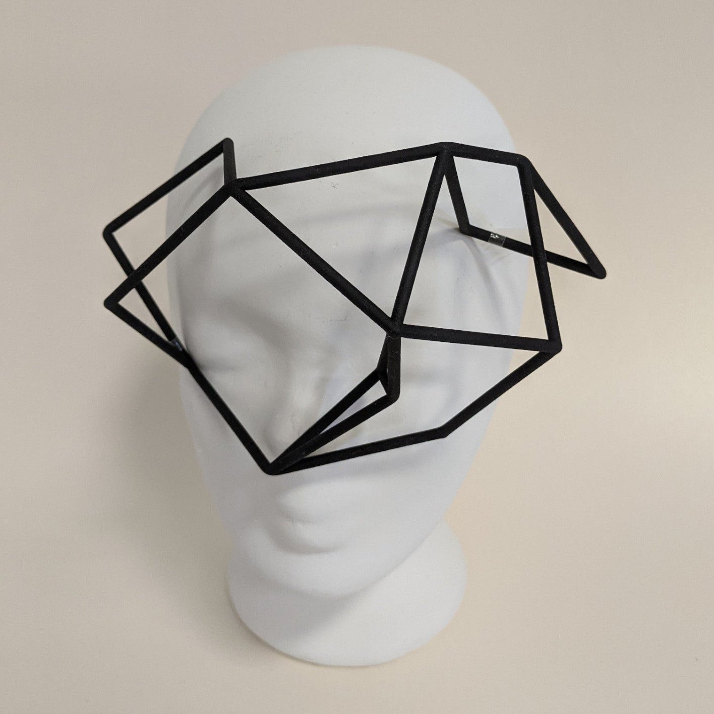 A geometric black frame resembling glasses sits on a white mannequin head, featuring an abstract, polygonal design.