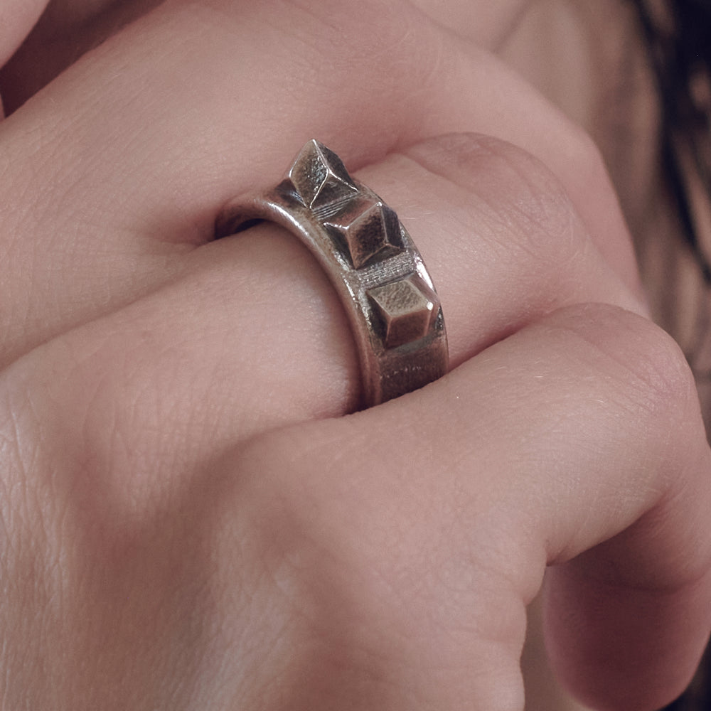 Close-up of a hand wearing a metallic ring featuring three raised geometric shapes on top.