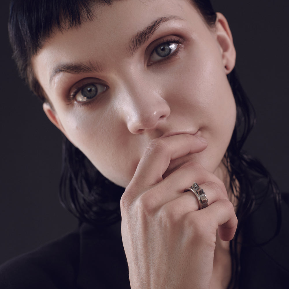 A close-up of a hand resting against a chin wearing a ring, showcasing delicate features and smooth skin against a dark background.