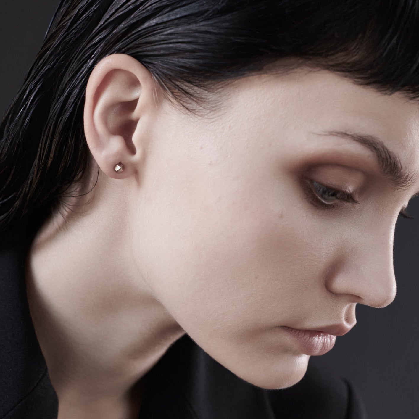 Close-up of a sleek, straight hair, highlighting a delicate ear adorned with a small stud earring against a dark background.