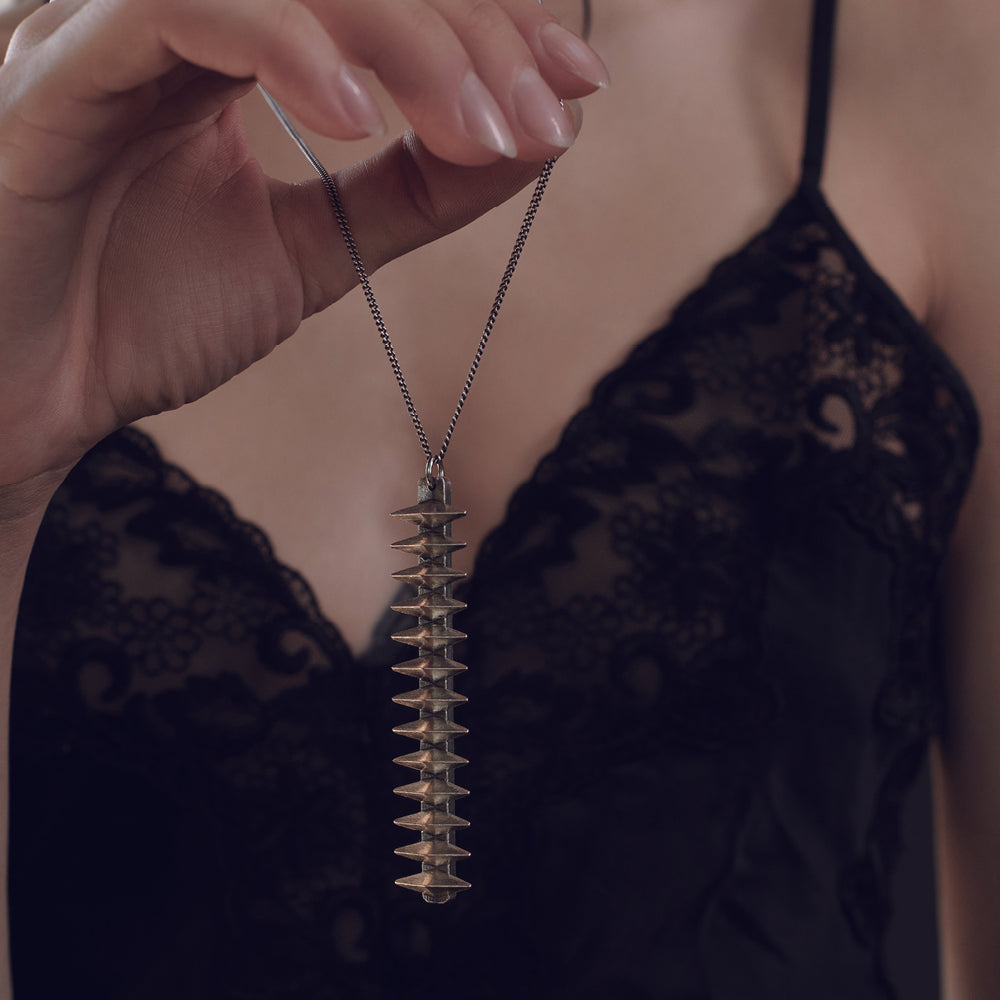Close-up of a hand holding a unique metallic spike pendant, wearing a black lace top, highlighting the intricate design of the necklace.