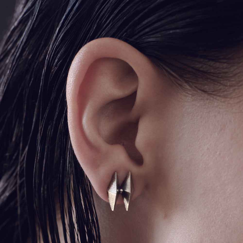 Close-up of a woman's ear adorned with geometric silver earrings, highlighting sleek design and textured hair.