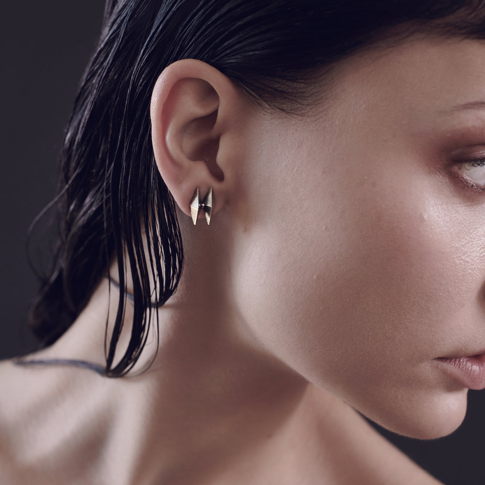 A close-up of an elegant ear displaying stylish gold earrings, with sleek black hair cascading down the side.