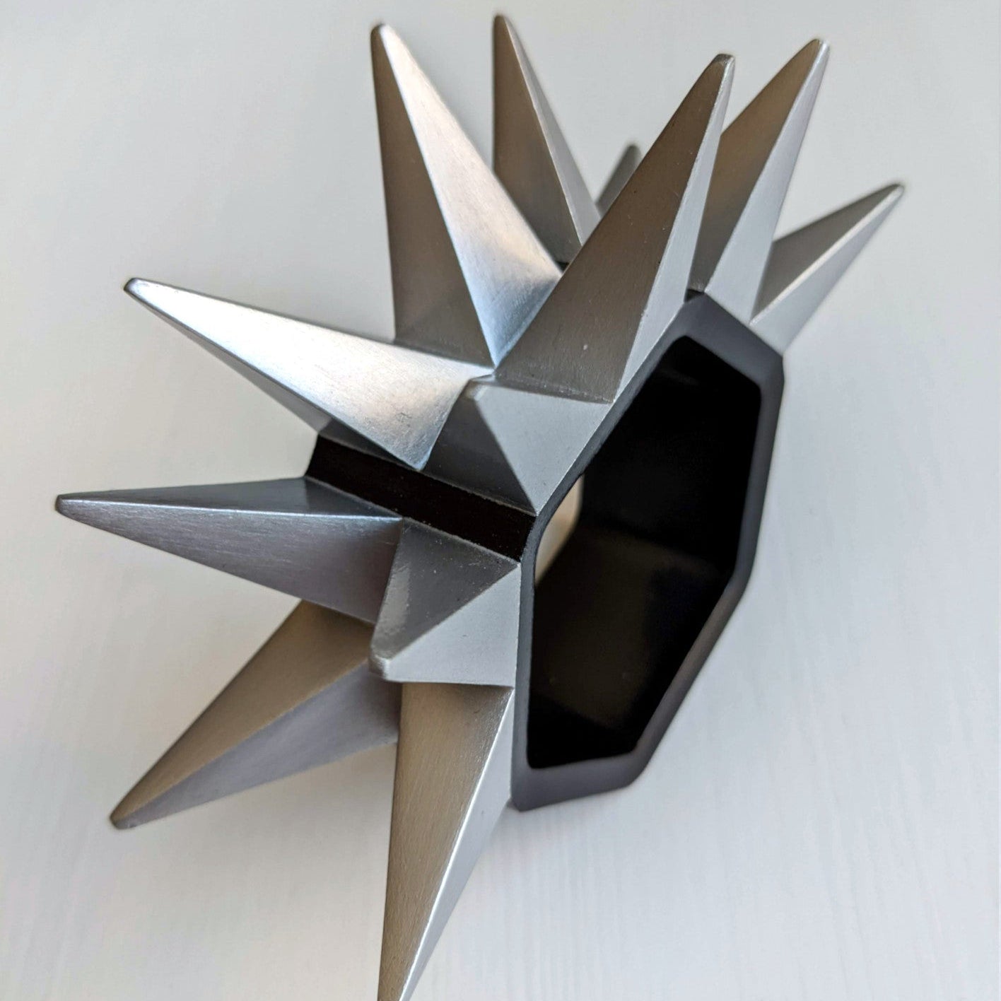 A metal ring with sharp, angular spikes extends outward from a hexagonal base, set against a light surface.