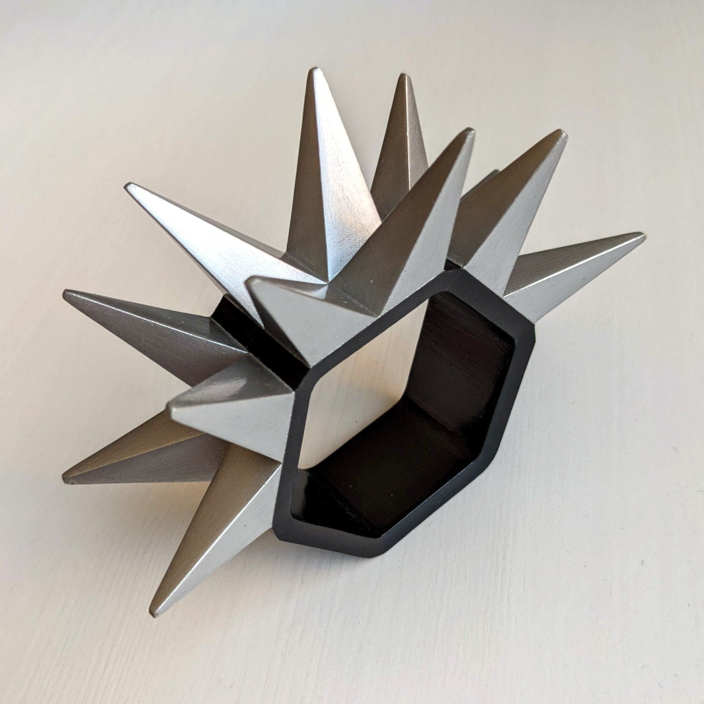 A metal ring with sharp, angular spikes extends outward from a hexagonal base, set against a light surface.