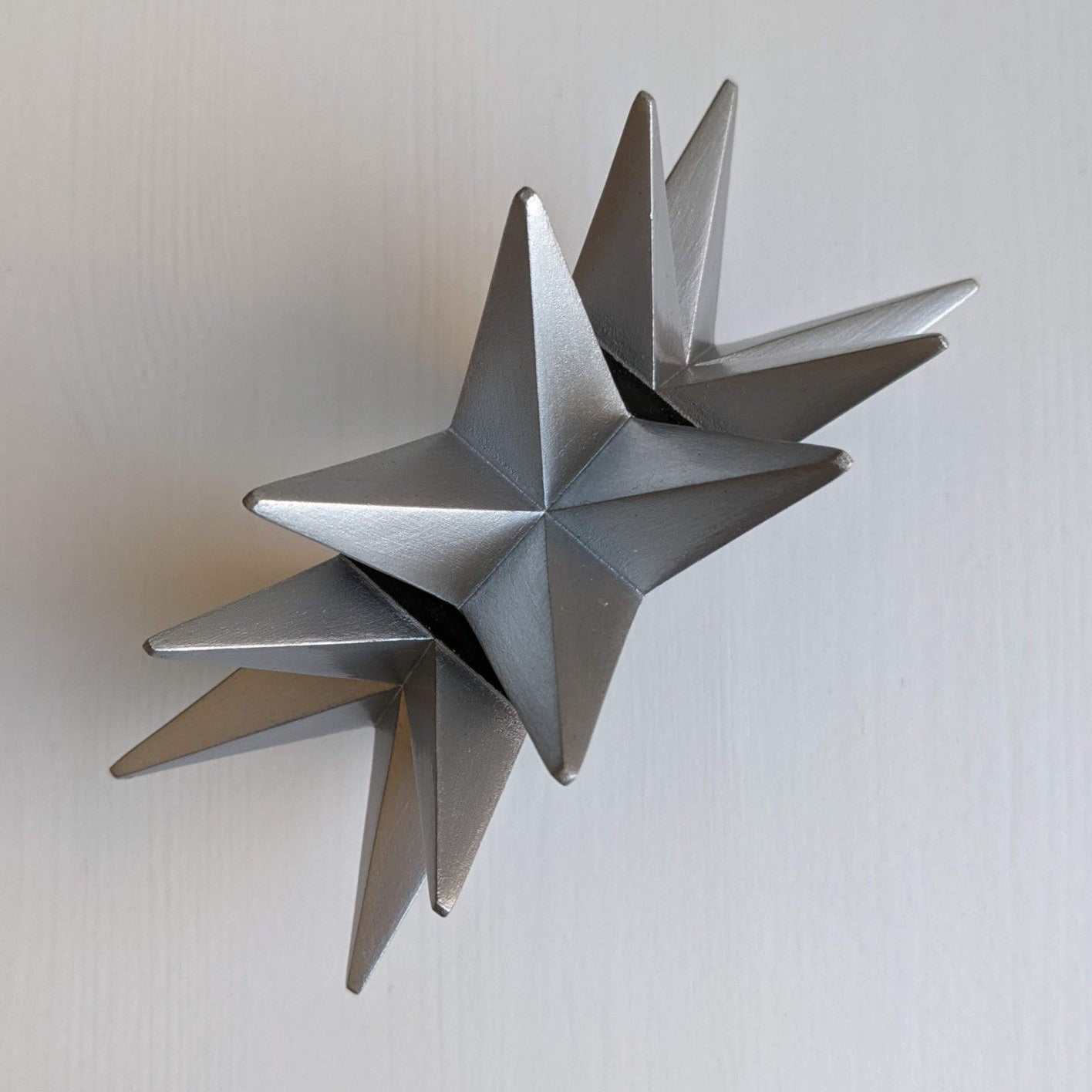 A silver, geometric star sculpture with multiple pointed spikes arranged symmetrically, set against a white background.