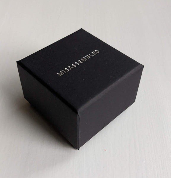 Close-up of a small black square box with the word "MISASSEMBLED" in all caps embossed in silver on the lid.