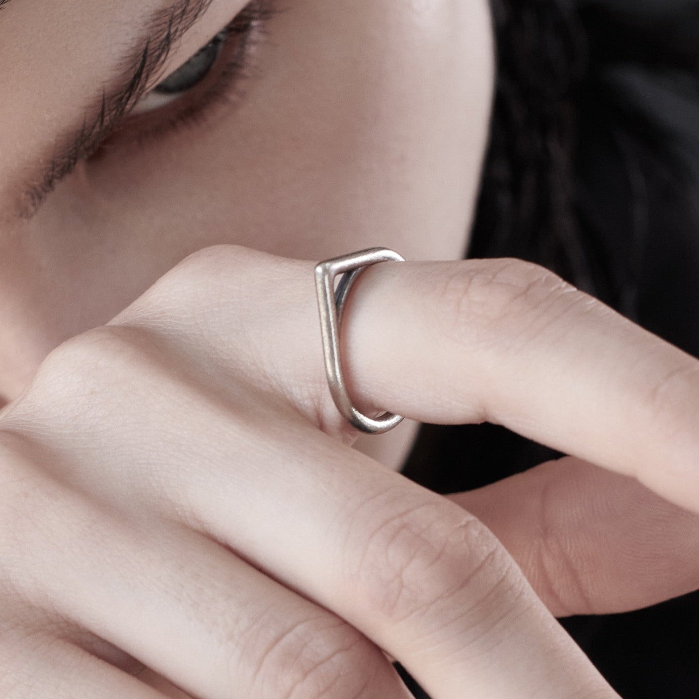 Close-up of a hand delicately holding a modern, minimalist silver ring, showcasing its sleek design against a dark background.