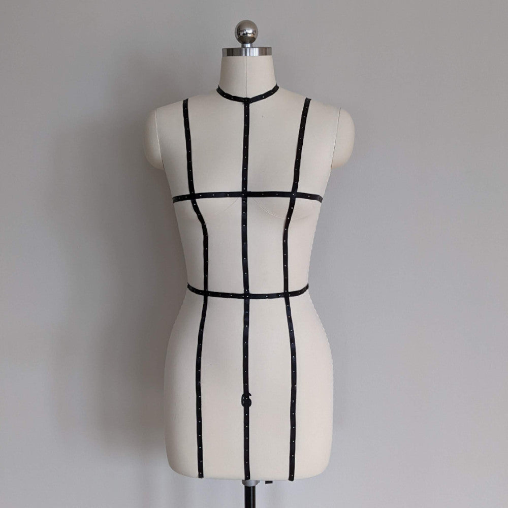 A tailored dress form with black grid lines, positioned on a stand against a plain gray background, ideal for fashion design.