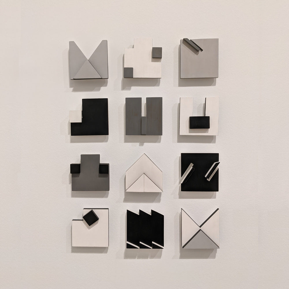 A grid of abstract geometric wall art in shades of black, white, and gray, featuring various shapes and arrangements.