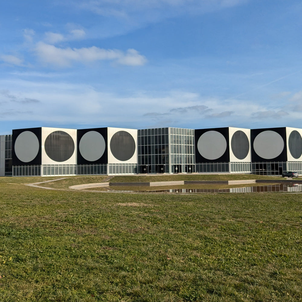 Modern building with large white circles on a black facade, surrounded by green grass and a clear blue sky.