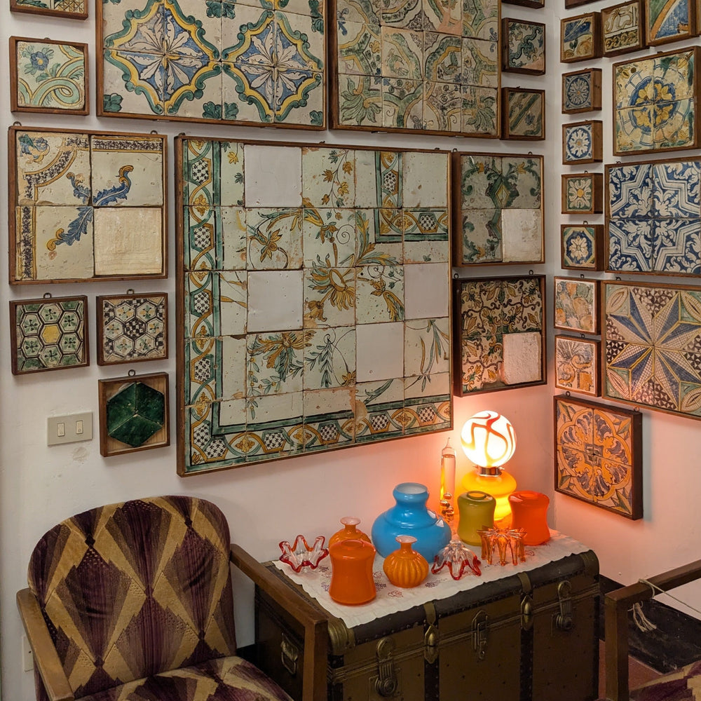 A cozy corner featuring a chair, stained glass artifacts, and a wall adorned with colorful ceramic tiles and framed art.